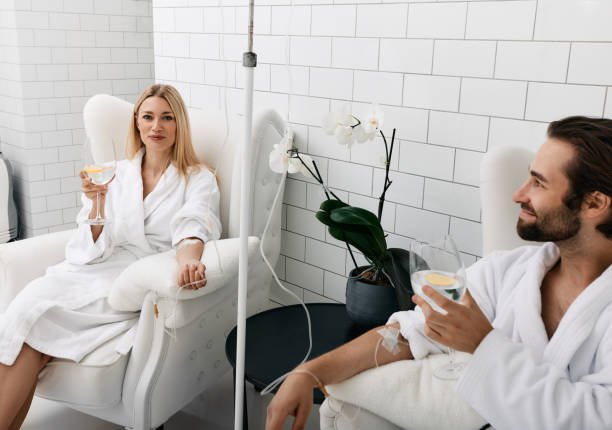 Couple in love during intravenous vitamin therapy. Beautiful woman with her boyfriend with glasses of refreshing drink with lemon in medical clinic for detox their organisms